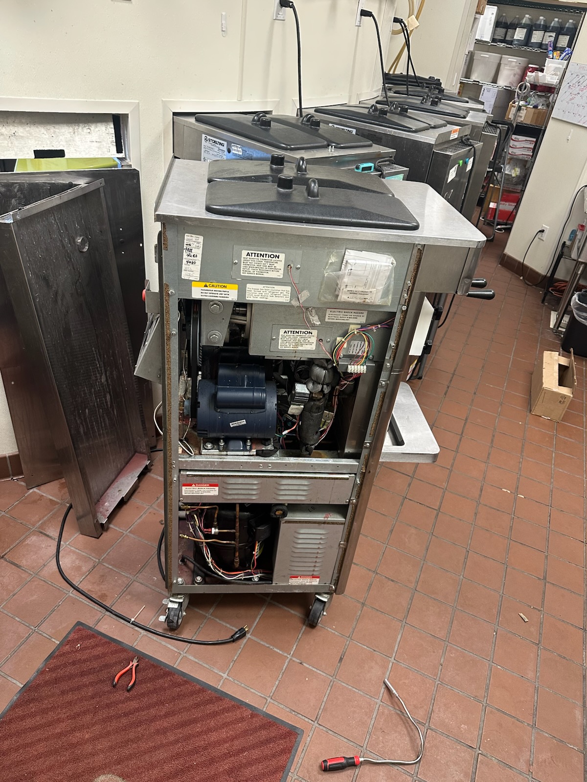 Stoelting frozen yogurt machine rear panel open showing compressor, motor, and refrigeration lines during repair